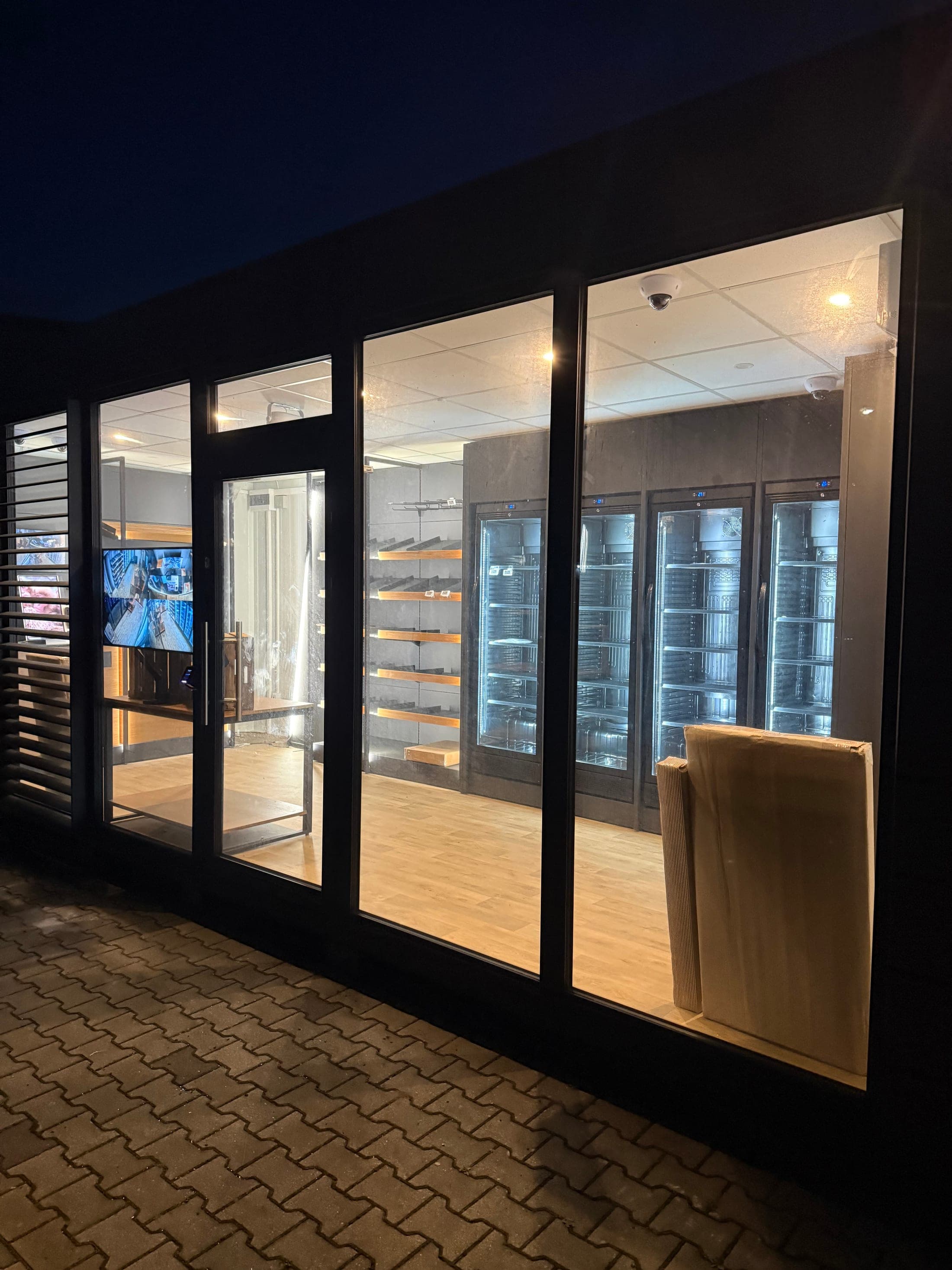Seitlicher Blick auf die beleuchtete Glasfront des 24/7-Shop-Containers bei Nacht