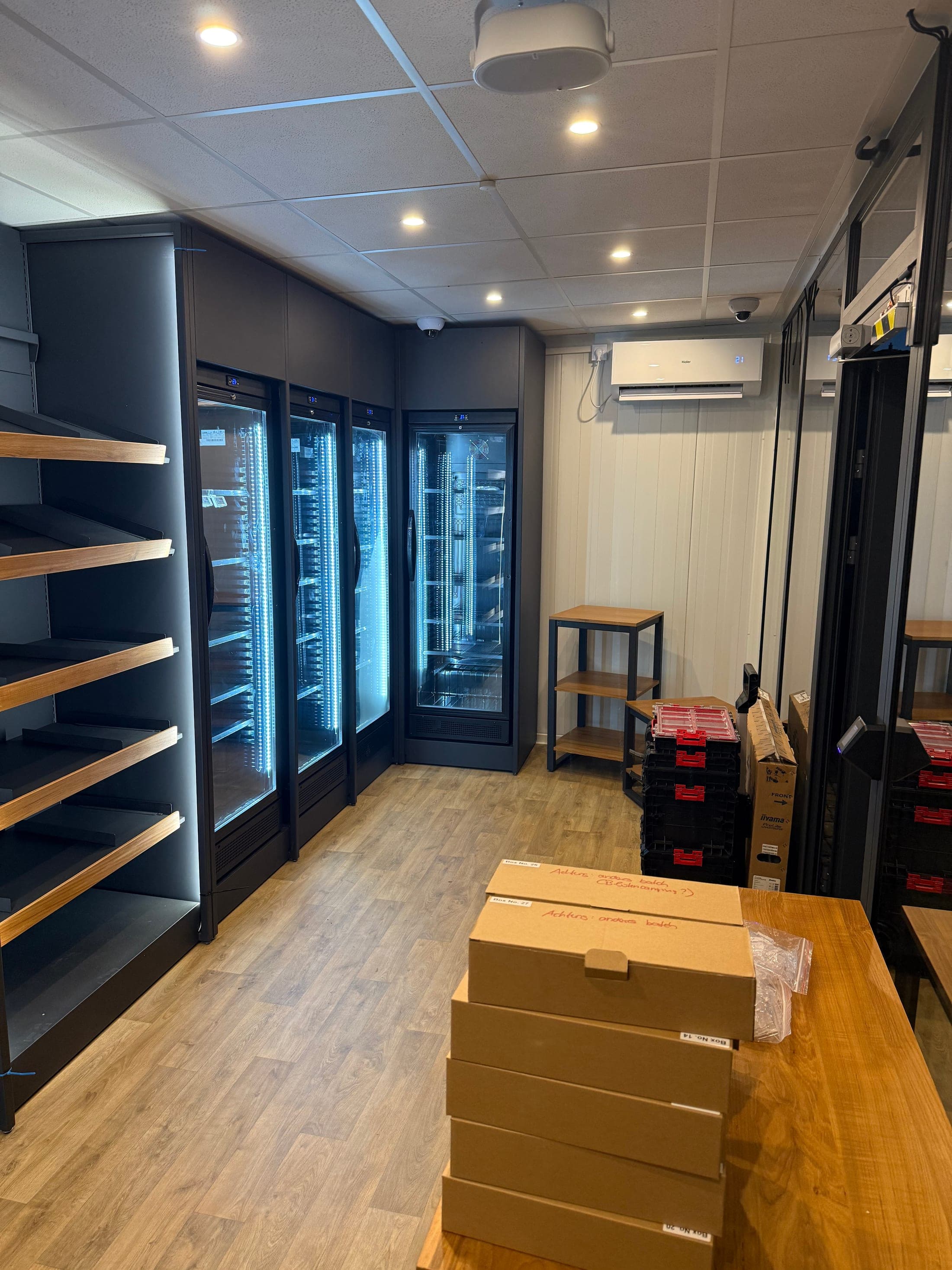 Innenausbau des Shop-Containers — Kühlschränke und Tiefkühltruhen mit LED-Beleuchtung, Holzregale und noch unausgepackte Kartons